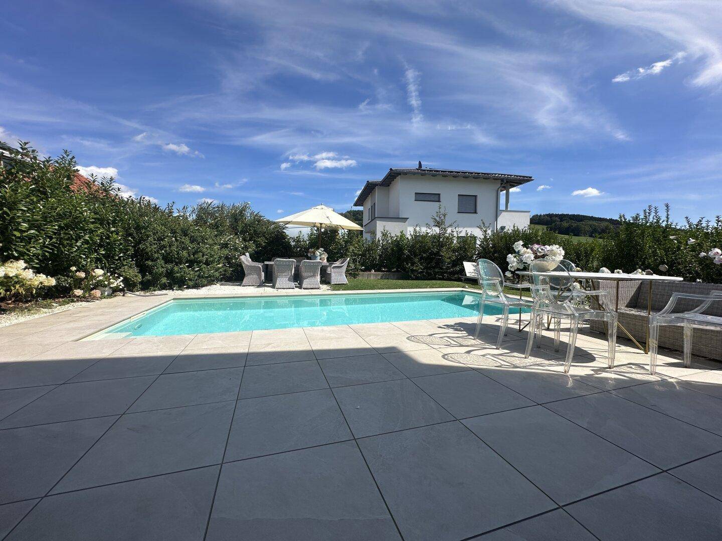 Sonniger Außenbereich mit Pool, großer Terrasse und Gartenmöbeln, ideal zum Entspannen.
