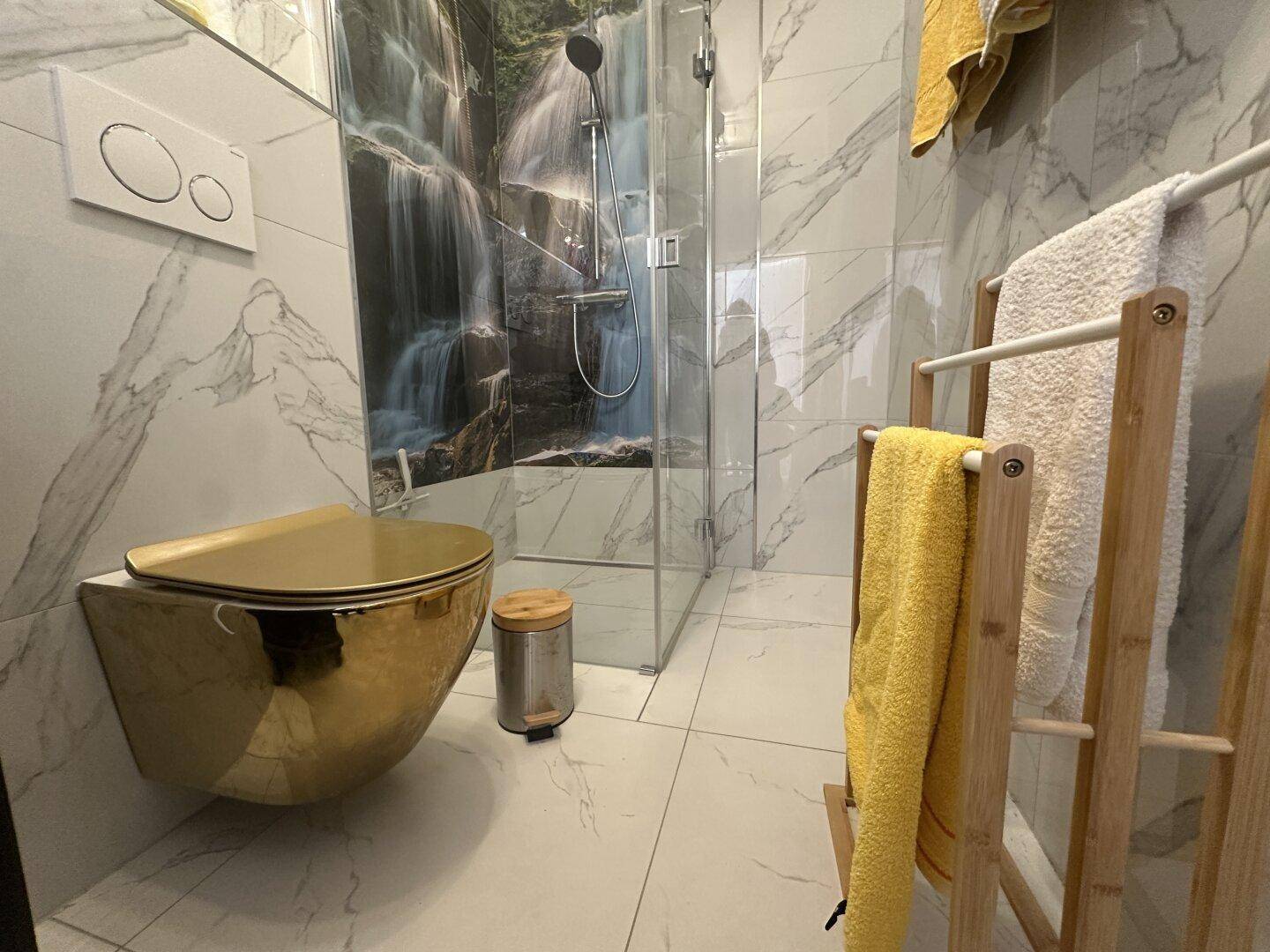 Exklusives WC mit goldener Toilette, Marmorfliesen und einer begehbaren Dusche im Hintergrund.