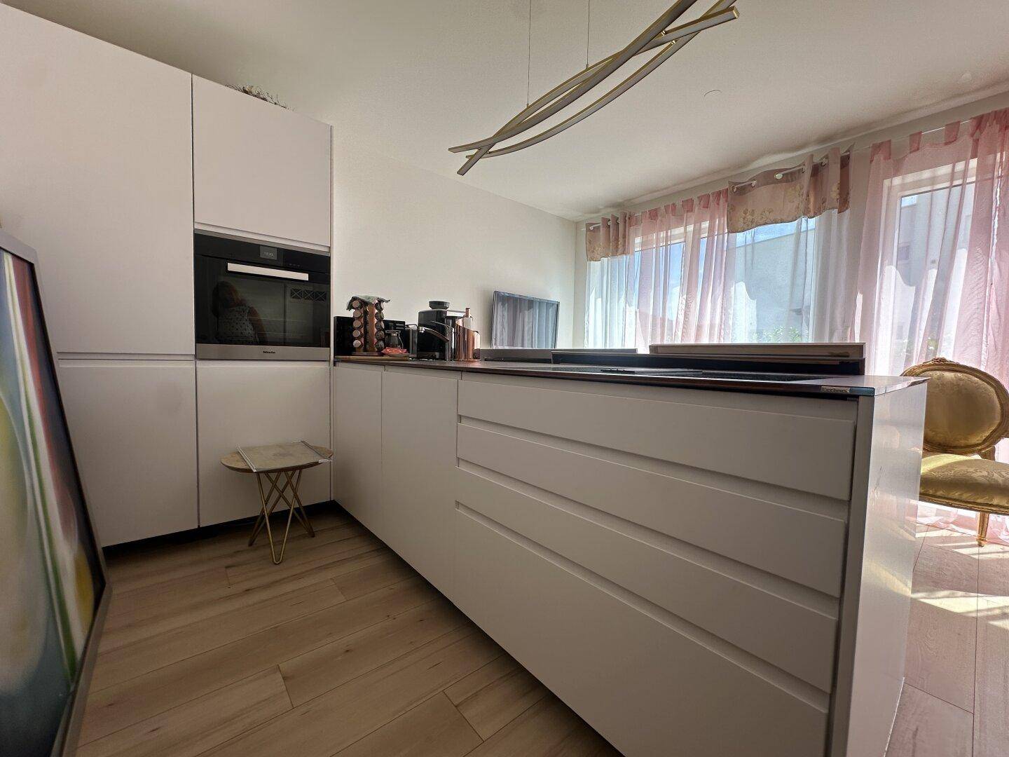 Moderne Küchenzeile mit weißen Schränken, integriertem Backofen und Kochinsel im offenen Wohnbereich.