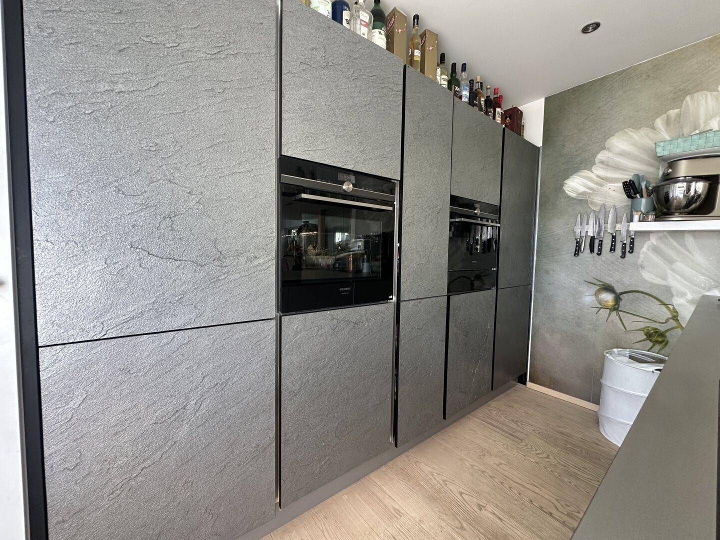 Moderne Küche mit grauen Schieferfronten, integrierten Backöfen und Holzfußboden.