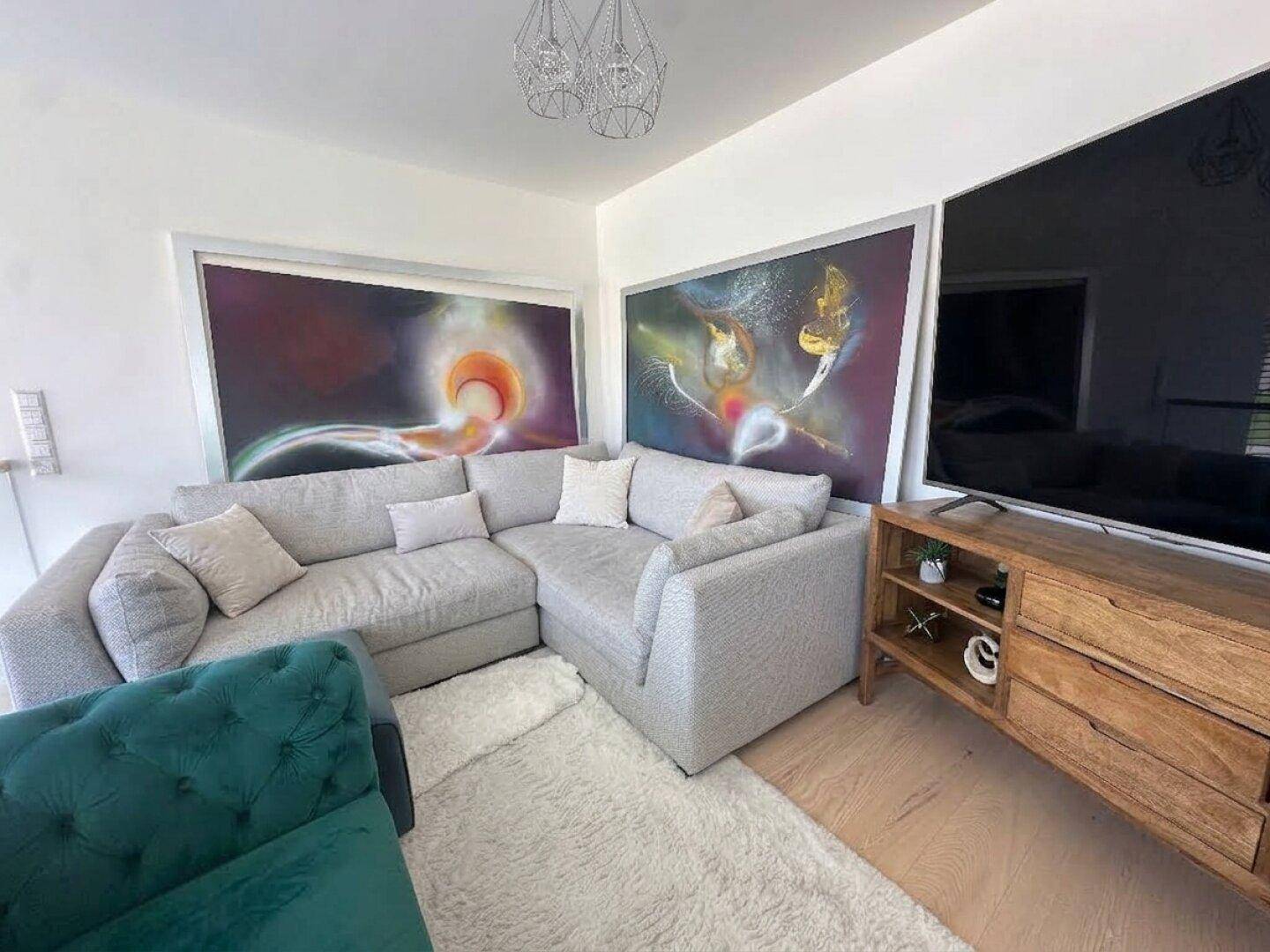 Gemütliches Wohnzimmer mit Ecksofa, Teppich und modernen Kunstwerken an den Wänden.