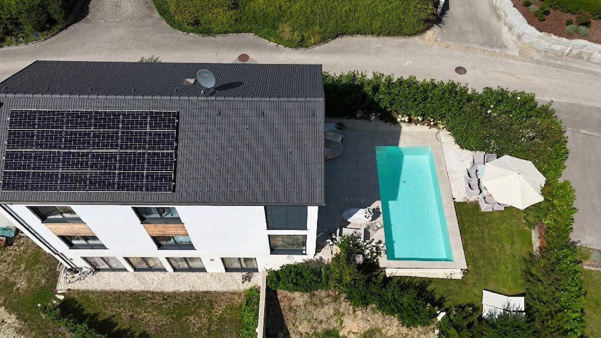 Luftaufnahme eines modernen Hauses mit Photovoltaikanlage auf dem Dach und privatem Pool.