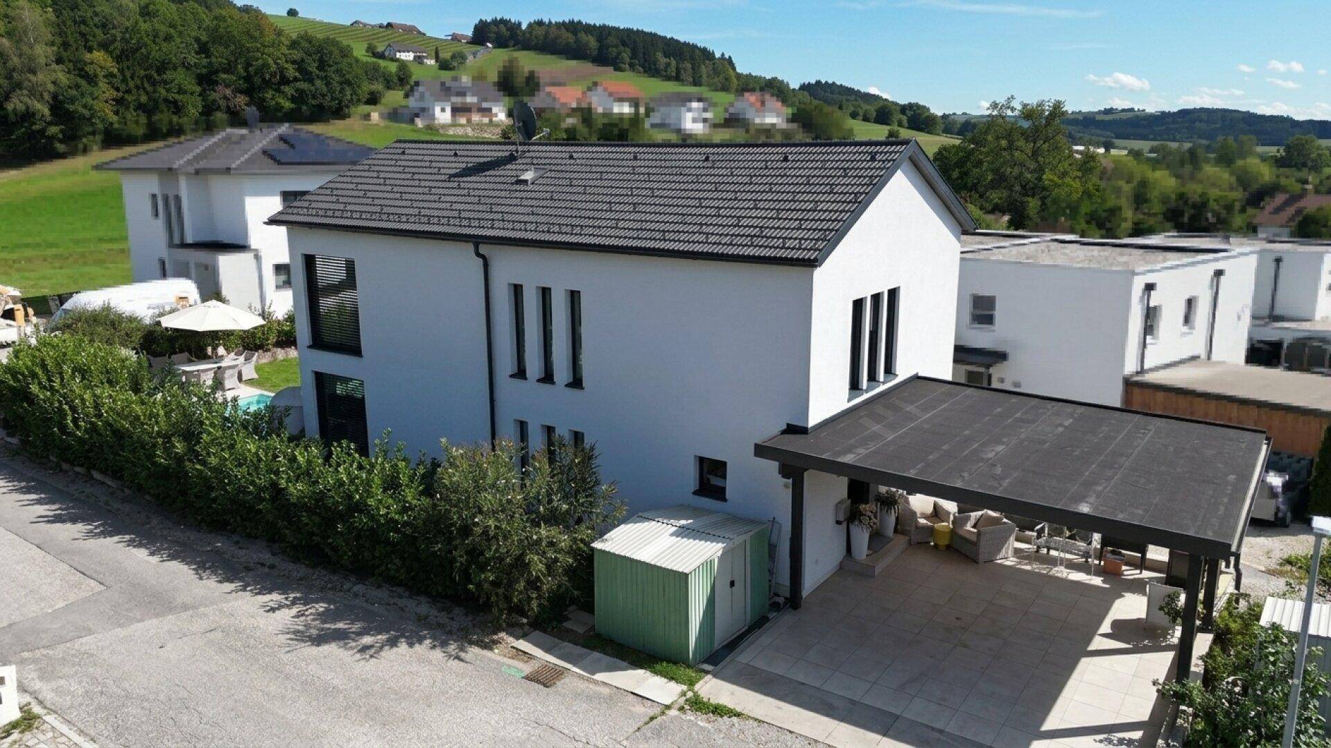 Luftaufnahme eines modernen Hauses mit Carport, Garten und Blick auf die umliegende Hügellandschaft.