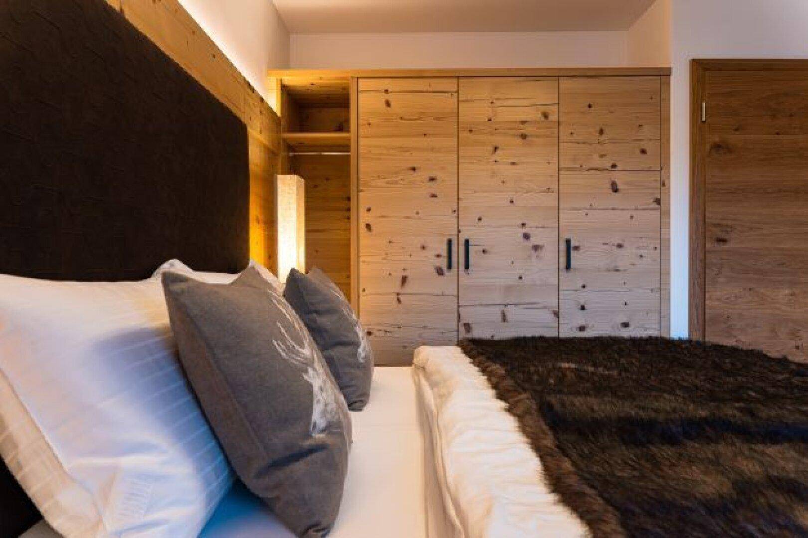 Schlafzimmer im alpinen Stil mit Holzeinbauschränken und gemütlichem Bett mit Fellüberwurf.