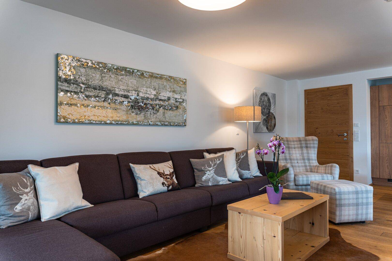 Gemütliches Wohnzimmer mit großem Ecksofa, Holztisch und Kissen mit Hirschmotiven im alpinen Stil.