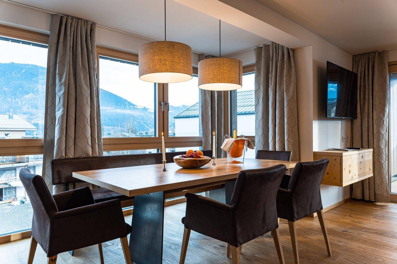 Heller Essbereich mit Holztisch, bequemen Stühlen und großen Fenstern mit Bergblick.