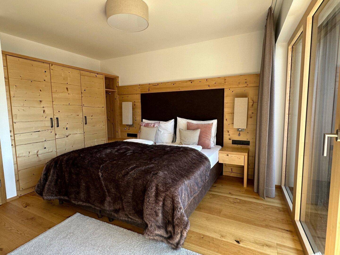 Helles Schlafzimmer mit Holzwänden, großem Bett und Zugang zu einem sonnigen Außenbereich.