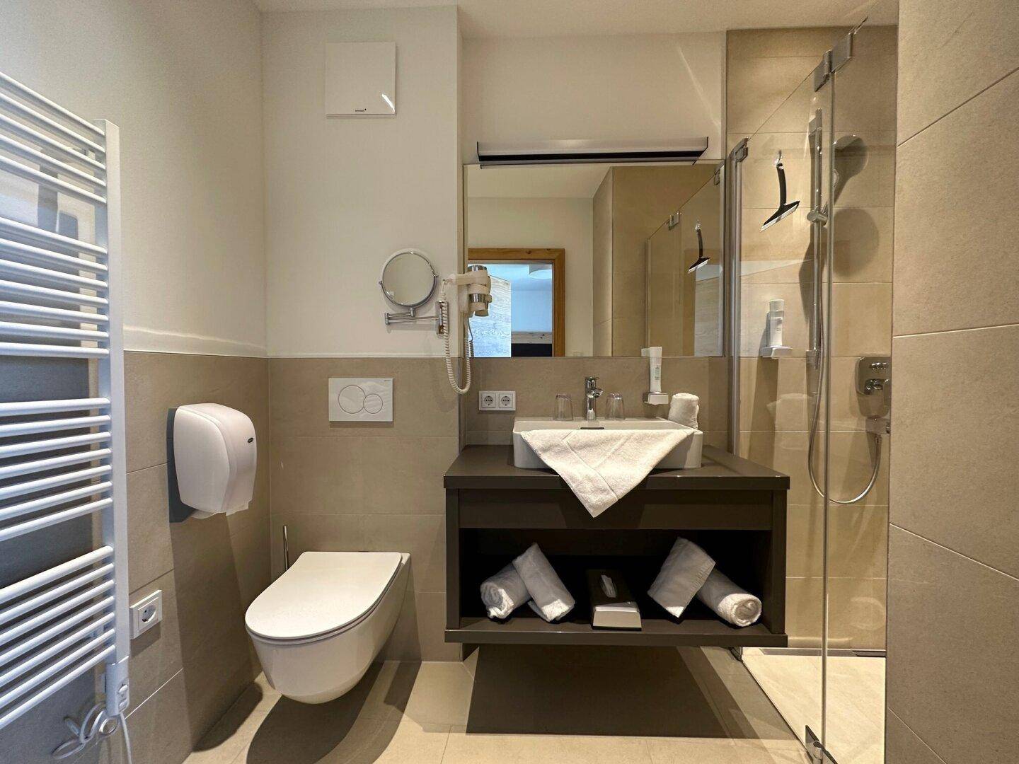 Modernes Badezimmer mit begehbarer Dusche, Wand-WC und praktischem beheiztem Handtuchhalter.