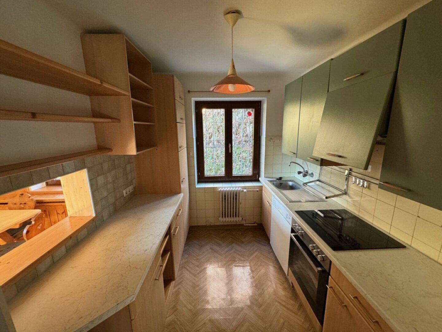 Funktionale Küche mit hellen Holzschränken, grünen Oberschränken und Fensterblick.