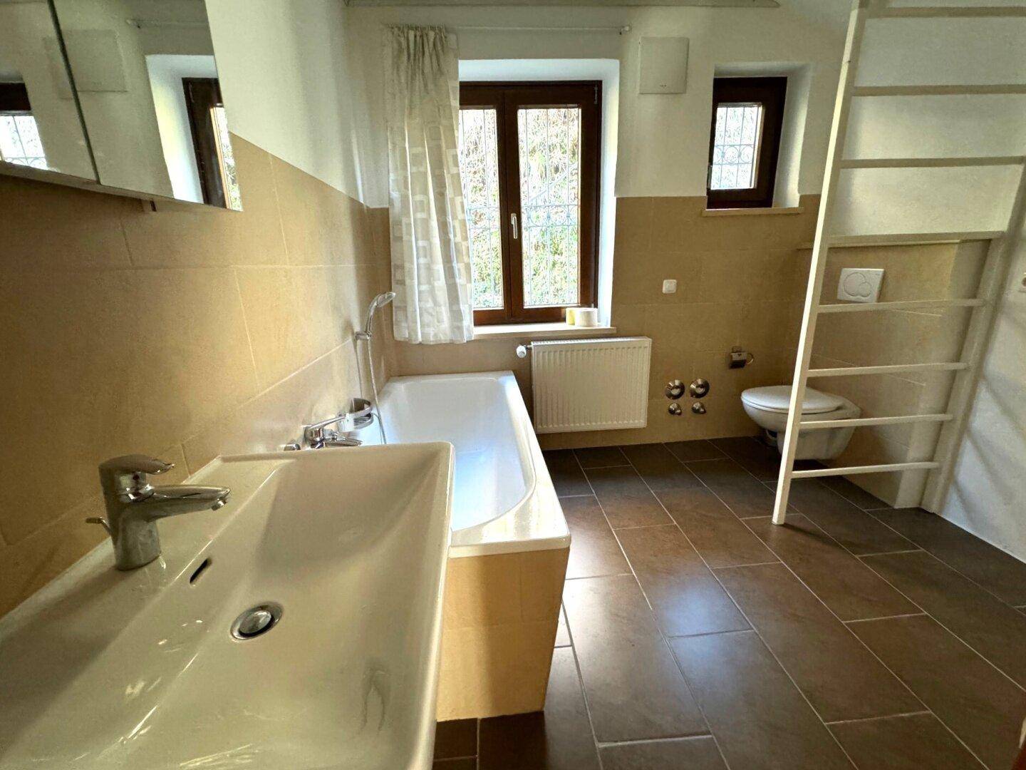 Badezimmer mit Badewanne, Einzelwaschbecken, WC und Fenster für Tageslicht.