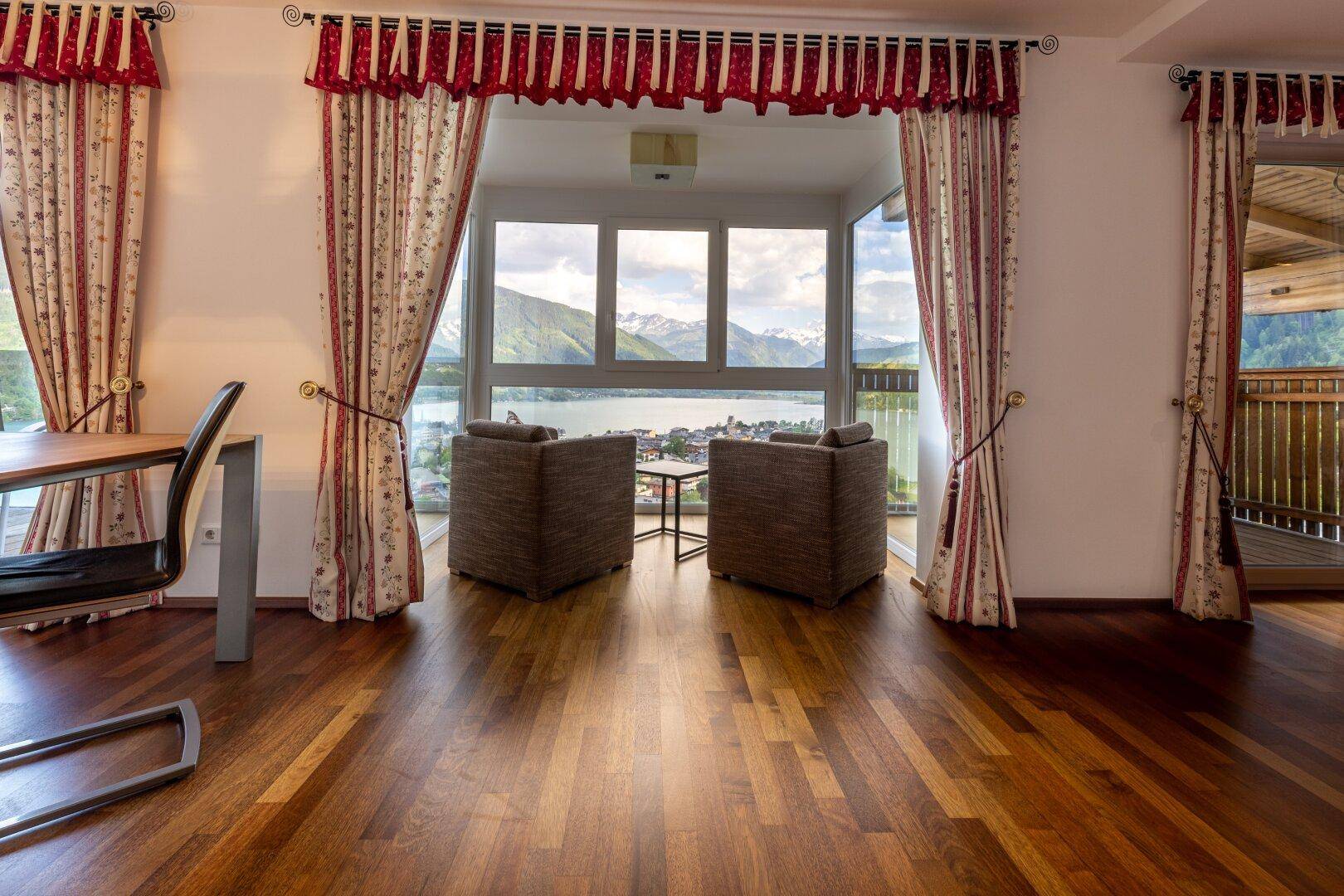 Geräumiges Wohnzimmer mit Holzboden, gemütlichen Sesseln und einem atemberaubenden Blick auf den See und die Berge.