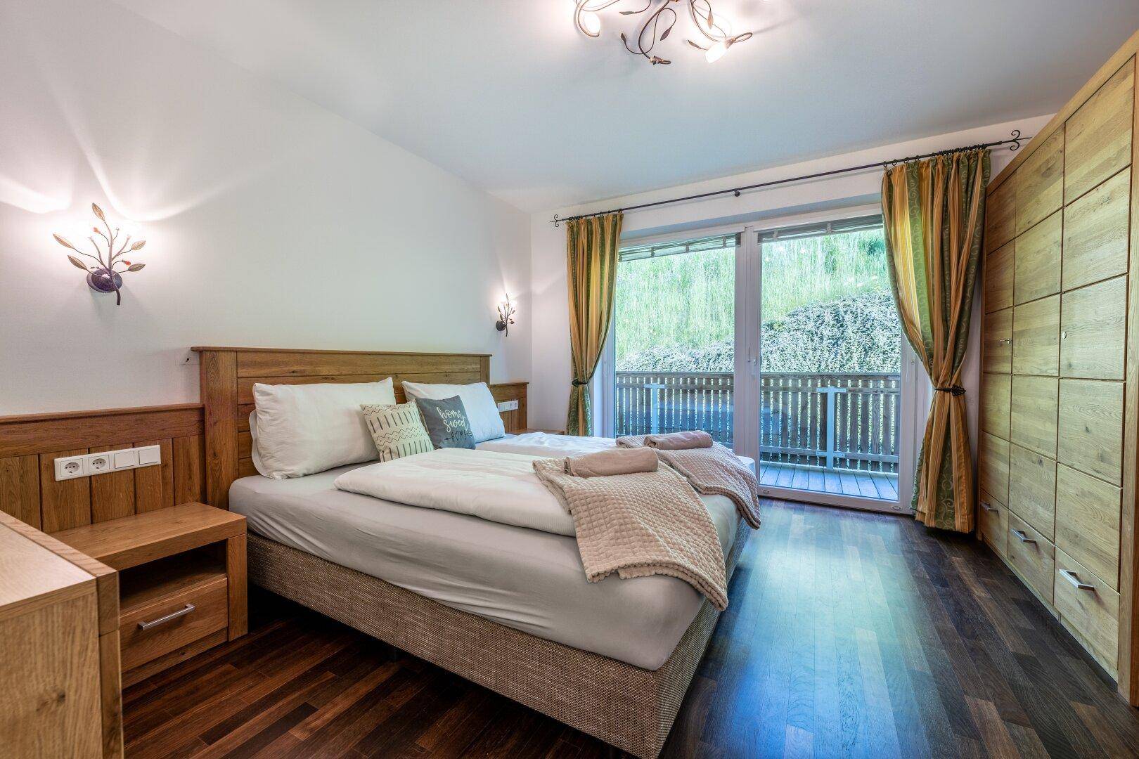 Gemütliches Schlafzimmer mit Holzbett, Einbauschränken und Zugang zu einem Balkon mit Blick ins Grüne.