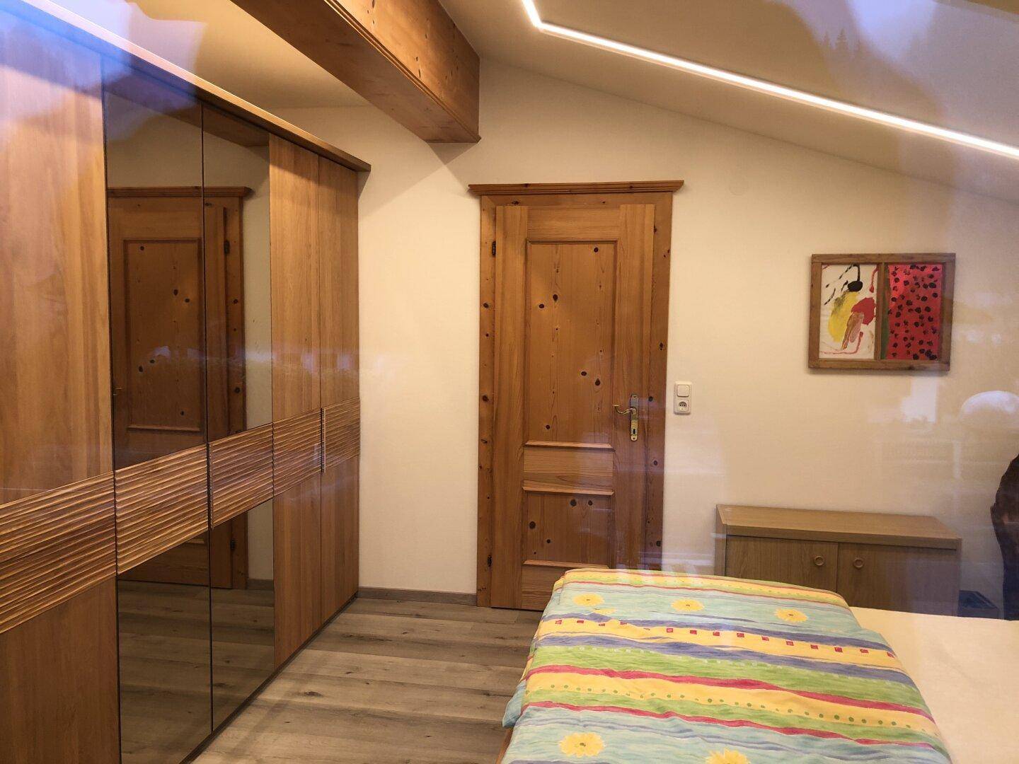 Schlafzimmer mit Holzbalken, Einbauschrank mit Spiegelfronten und schräger Decke.
