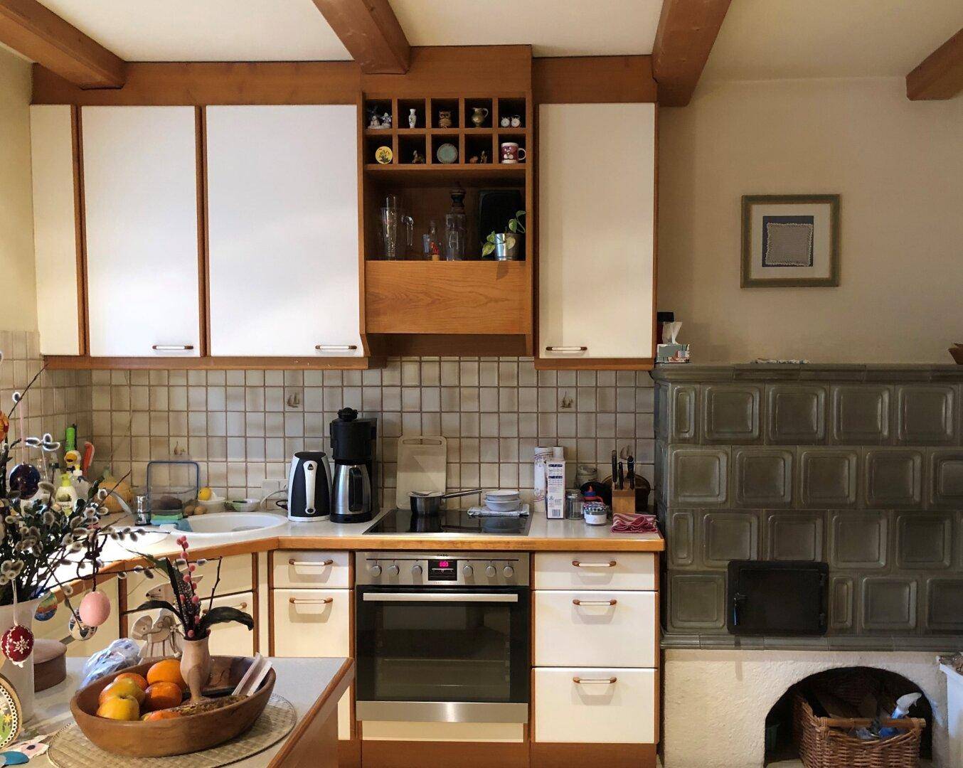 Funktionale Küche im Landhausstil mit integriertem Kachelofen, hellen Schränken und Fliesenboden.