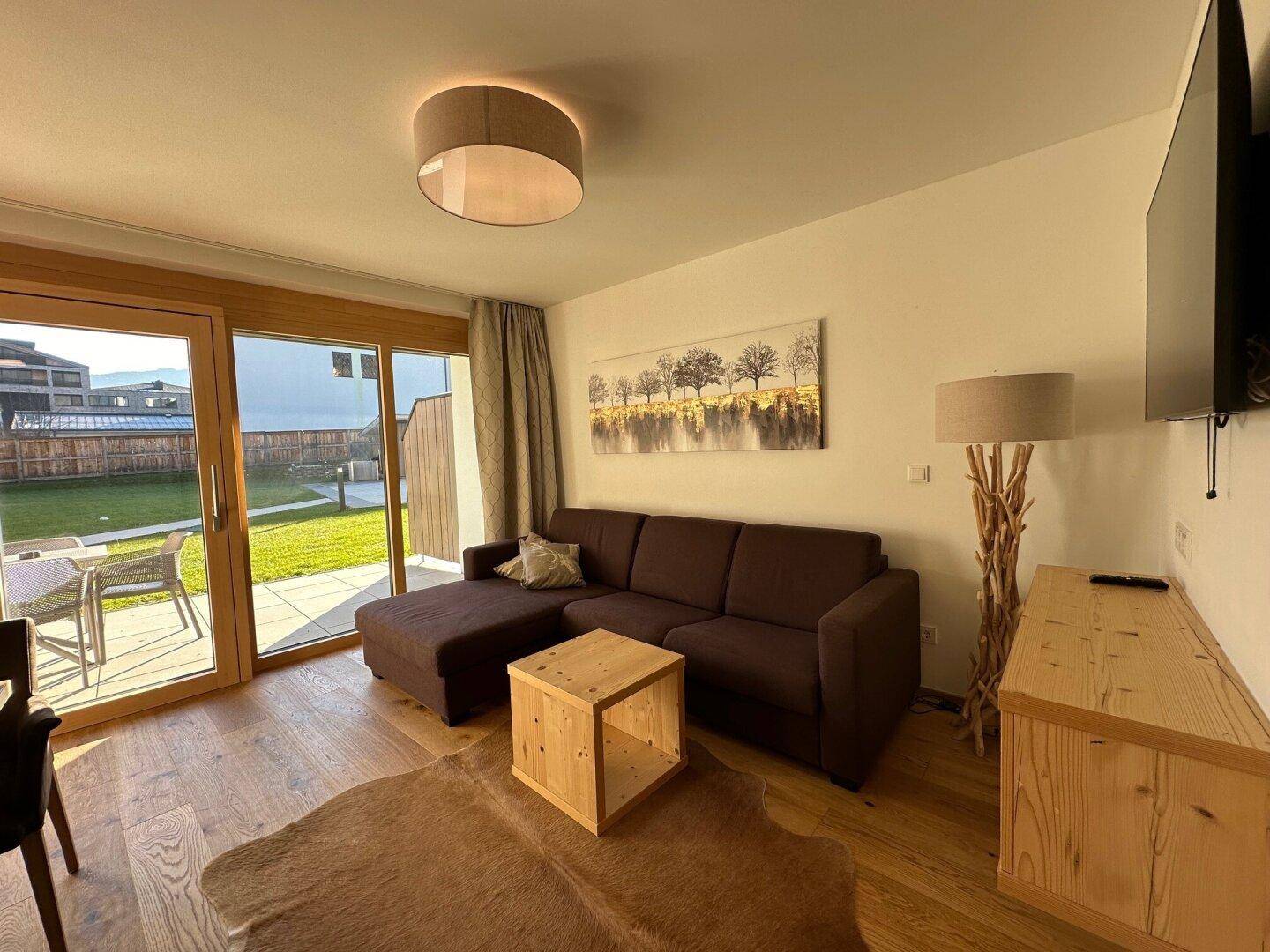 Gemütliches Wohnzimmer mit Sofa, Holzboden und direktem Zugang zur Terrasse und Garten.