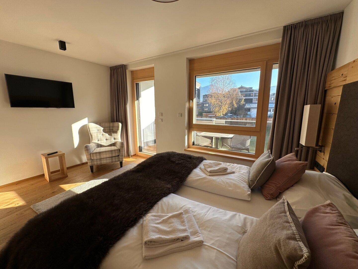 Sonniges Schlafzimmer mit Doppelbett, Holzboden und Zugang zu einem Balkon oder Terrasse.