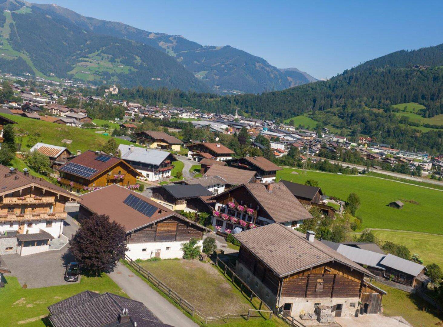 Luftaufnahme eines charmanten Dorfes in einem Tal, umgeben von majestätischen Bergen und grünen Wiesen.