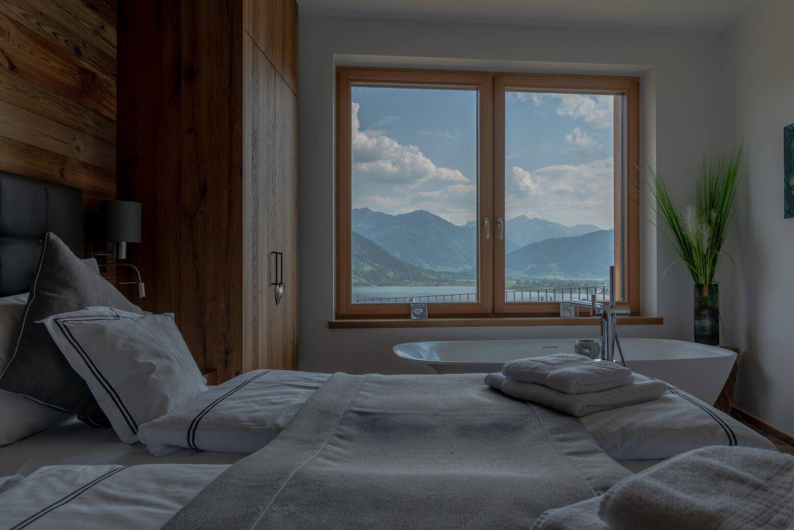 Schlafzimmer mit Doppelbett, Holzschrank und freistehender Badewanne am Fenster mit Seeblick und Bergsicht.