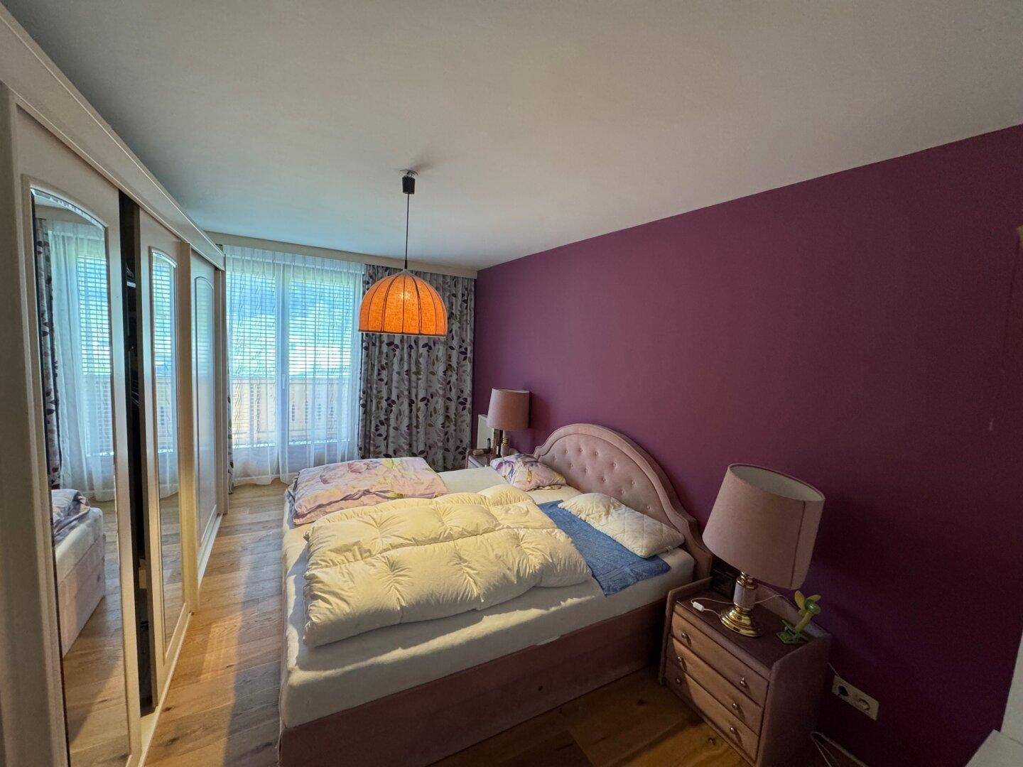 Gemütliches Schlafzimmer mit lila Akzentwand, Holzfußboden und großem Spiegelschrank.