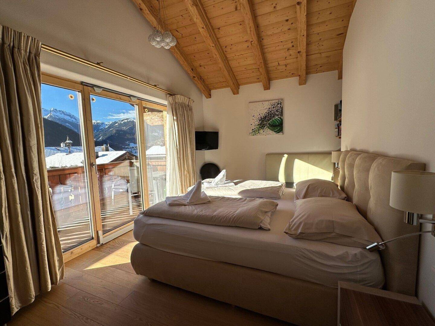 Gemütliches Schlafzimmer mit Holzbalkendecke, großem Bett und Balkonzugang mit Bergblick.