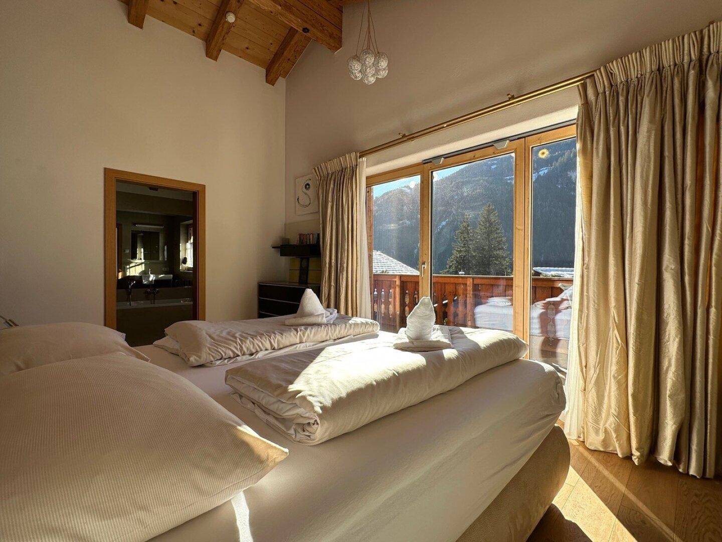 Lichtdurchflutetes Schlafzimmer mit Holzbalkendecke und weitem Bergblick durch große Fenster.