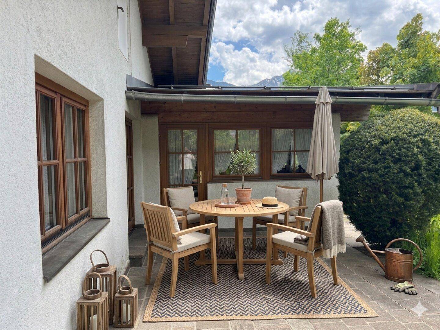 Gemütliche Terrasse mit Holztisch, Stühlen, Sonnenschirm und Blick auf die Berge.