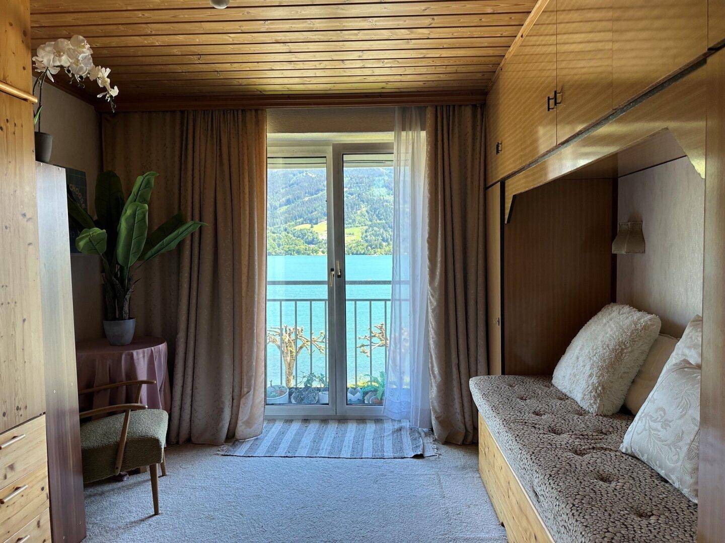 Gemütliches Schlafzimmer mit Holztäfelung, Seeblick und Zugang zu einem kleinen Balkon.
