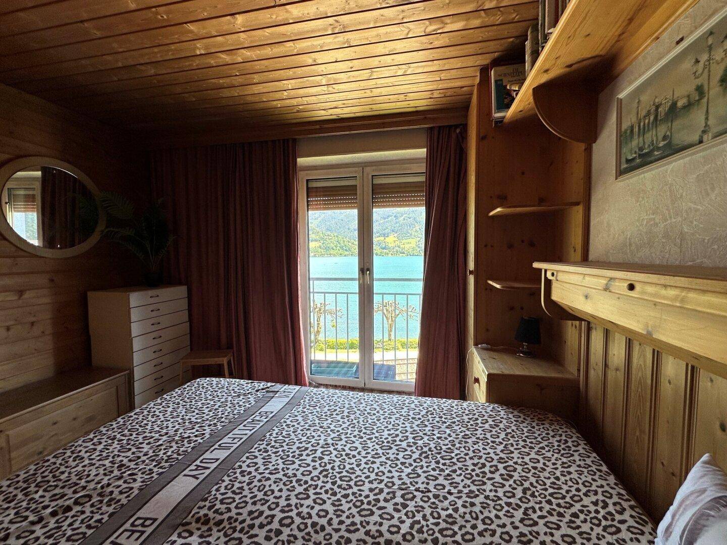 Rustikales Schlafzimmer mit Holzwänden, Leopardendruck-Bettwäsche und direktem Seeblick vom Balkon.