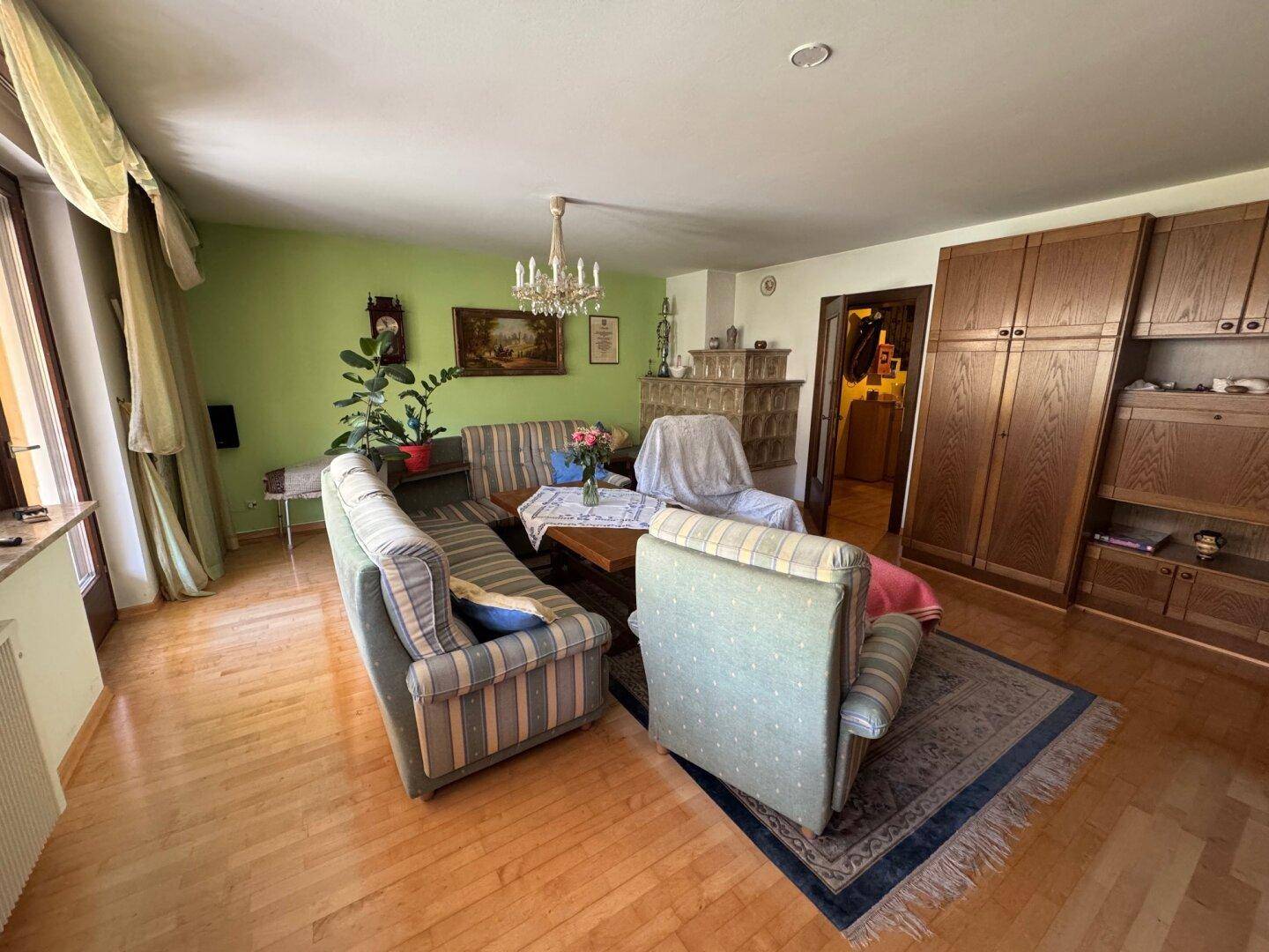 Gemütliches Wohnzimmer mit grün gestrichener Wand, Holzboden und traditionellem Kachelofen.
