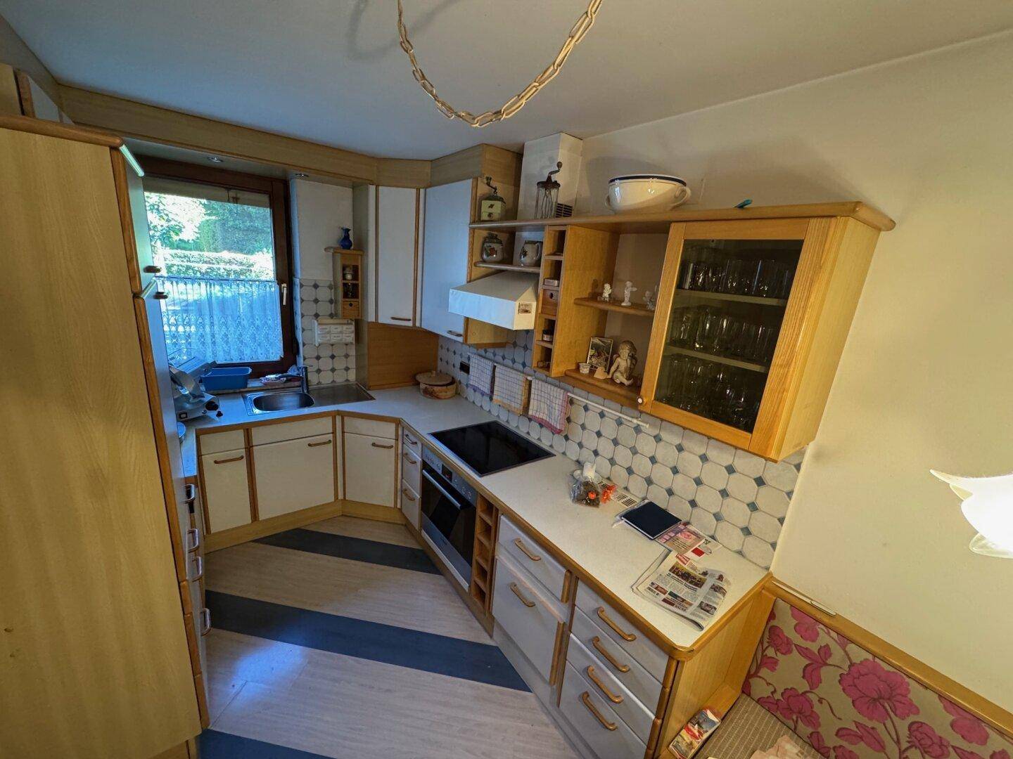 Traditionelle Einbauküche in Eckanordnung mit Holzschränken, gemusterten Fliesen und Fenster über der Spüle.
