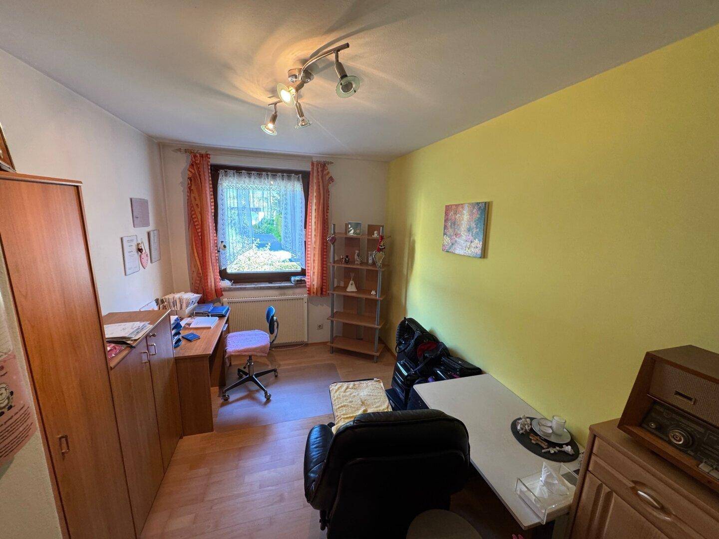 Funktionales Arbeitszimmer mit gelber Wand, Schreibtisch und Holzmöbeln, hell durch das Fenster.