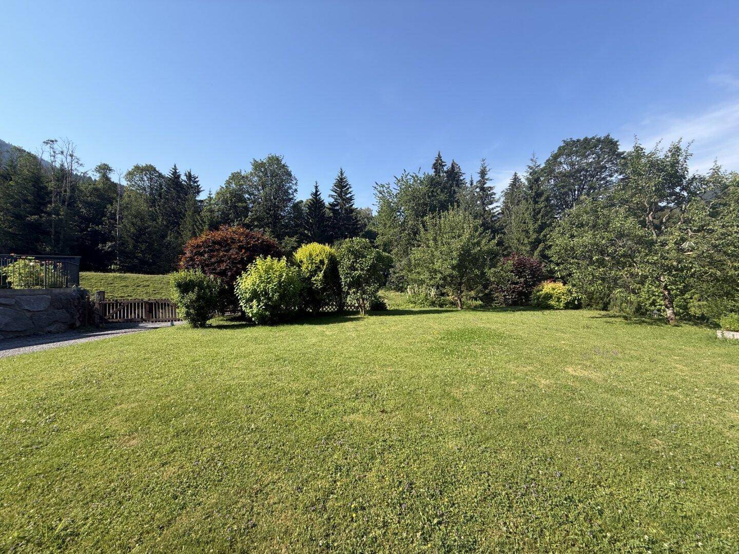 Großer, gepflegter Garten mit weitläufiger Rasenfläche und altem Baumbestand unter blauem Himmel.
