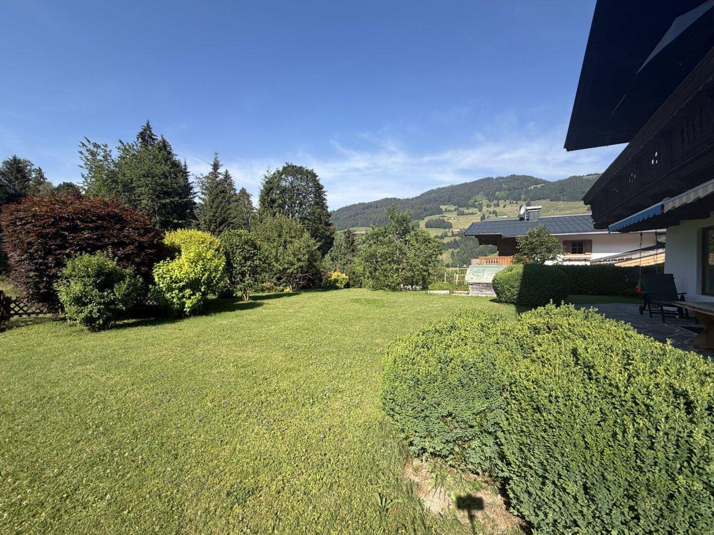 Weitläufiger Gartenbereich mit Rasen und Hecken, angrenzend an eine Terrasse mit Bergblick.