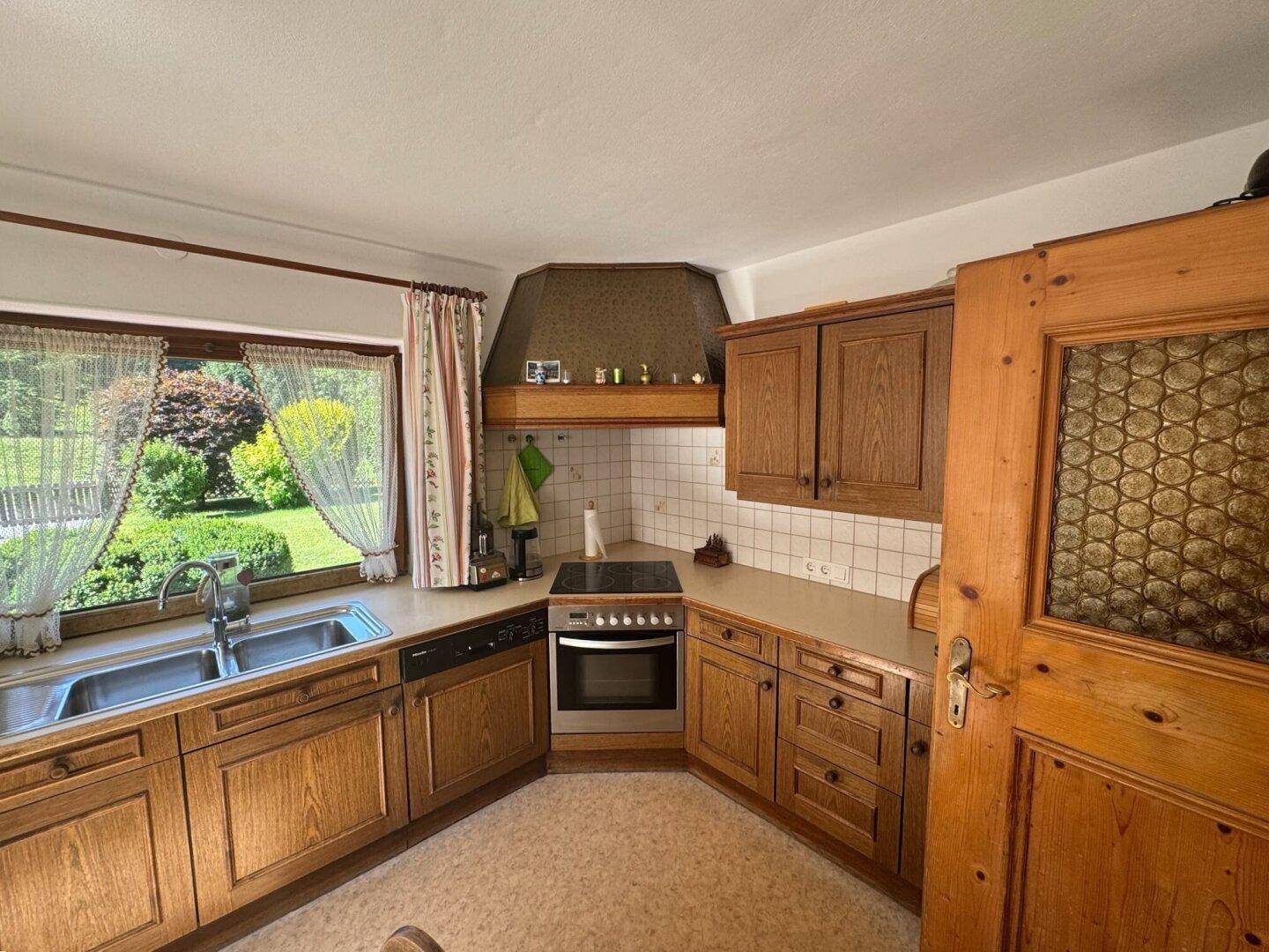 Traditionelle Holzküche mit Doppelspüle, Einbaugeräten und Fenster mit Blick ins Grüne.
