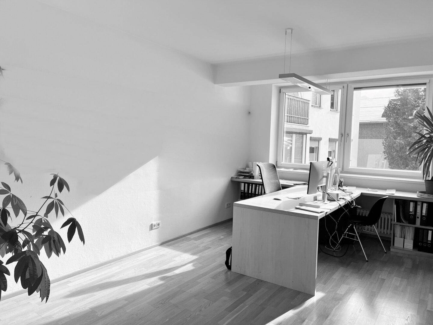 Helles Büro mit Holzboden und großen Fenstern, das viel Tageslicht hereinlässt.