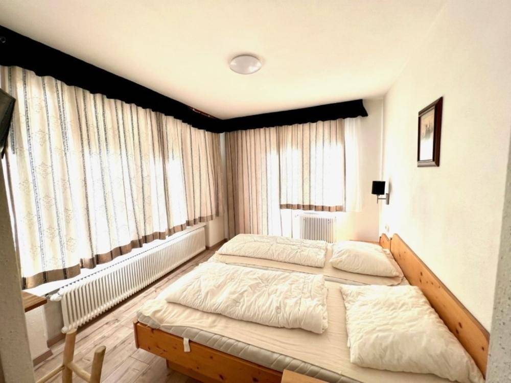 Gemütliches Schlafzimmer mit zwei Einzelbetten, großen Fenstern und hellen Vorhängen.