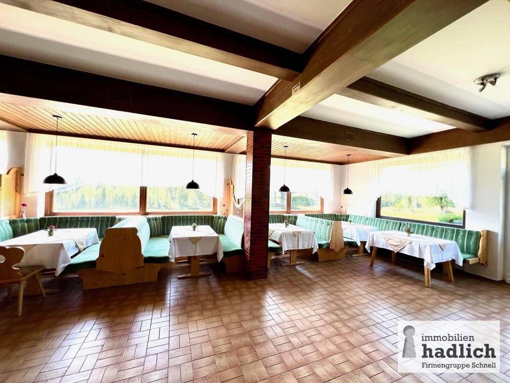 Großer Speisesaal mit gemütlichen Sitzbänken, Holzbalken an der Decke und weitem Blick ins Grüne durch die Fenster.
