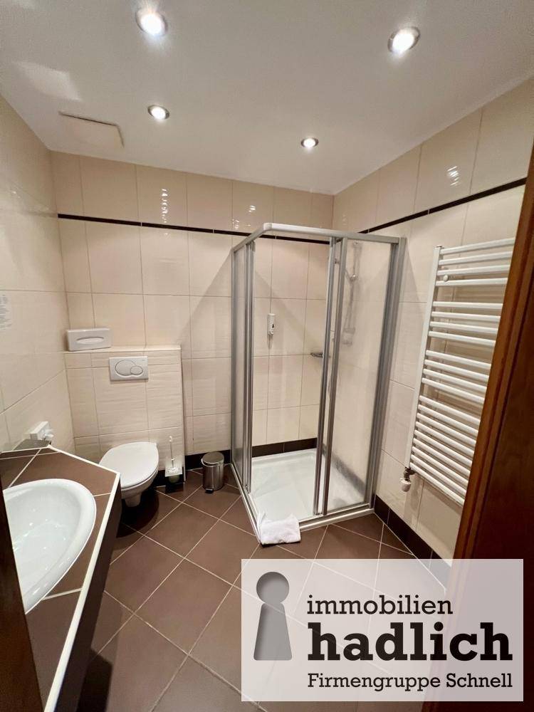 Modernes Badezimmer mit Duschkabine, WC, Waschbecken und einem praktischen Handtuchheizkörper, alles in hellen Fliesen gehalten.