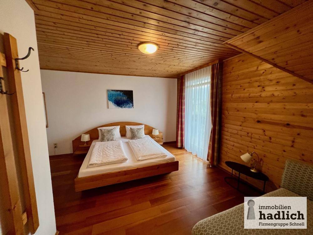 Helles Schlafzimmer mit Holzboden, Holzdecke und großer Fensterfront.
