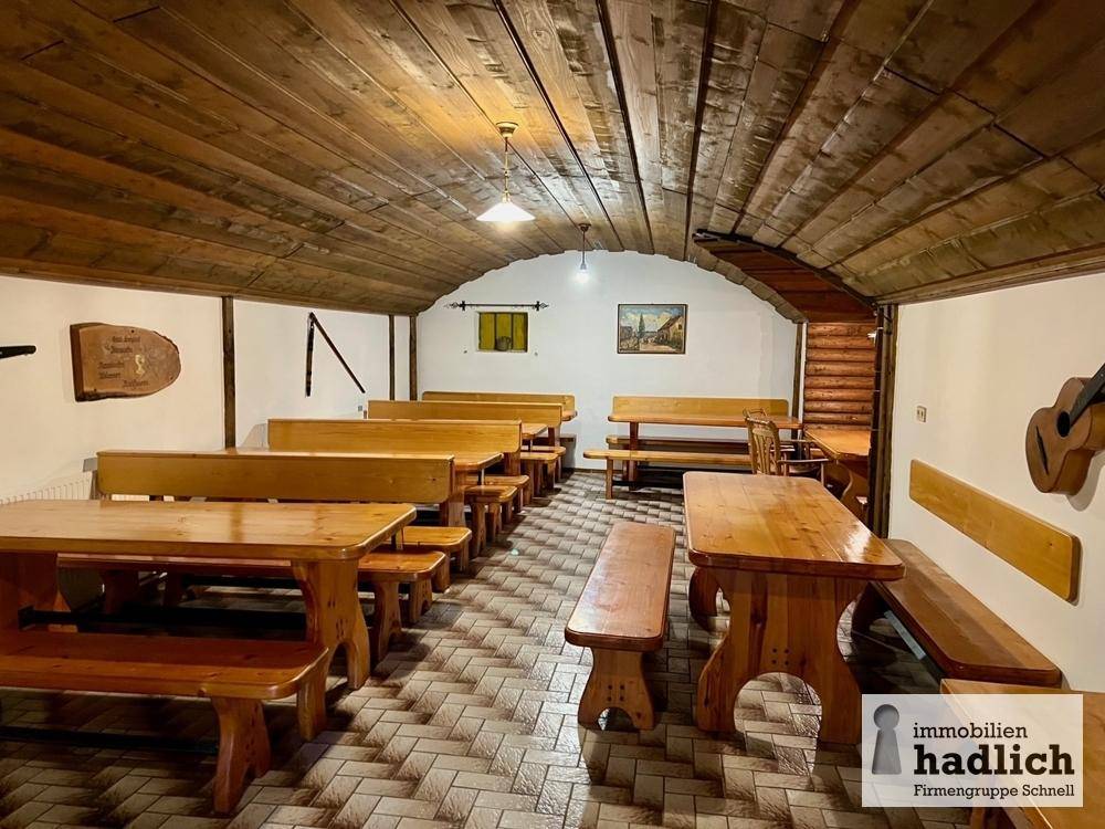 Rustikaler Gemeinschaftsraum mit Holzbänken, Tischen und gewölbter Holzdecke.