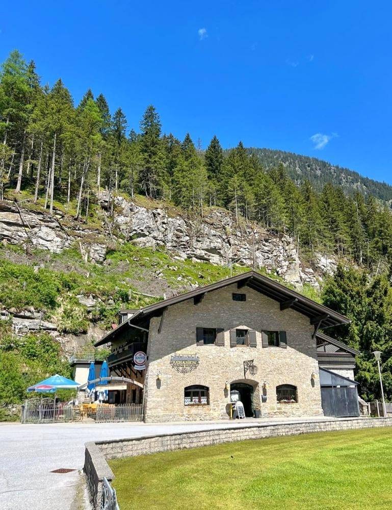 Traditionelles Steinhaus mit markanter Fassade und Fenstern, umgeben von grüner Natur und Bergen.