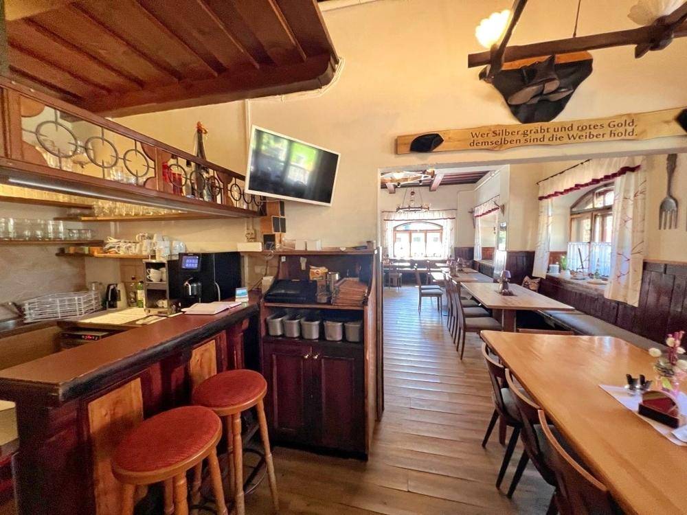 Gemütlicher Barbereich mit Holztresen, Barhockern und Regalen, der in den Speisesaal übergeht.
