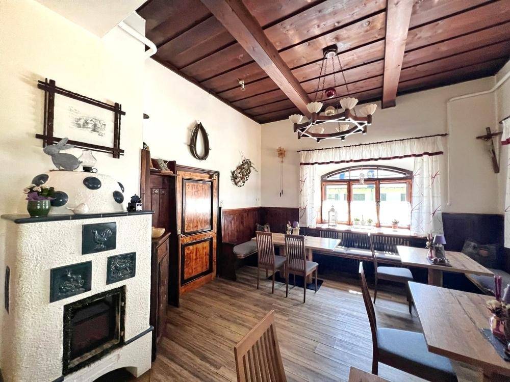 Weiterer Blick in den traditionellen Speisesaal mit mehreren Holztischen, Bänken und dem markanten Kachelofen.