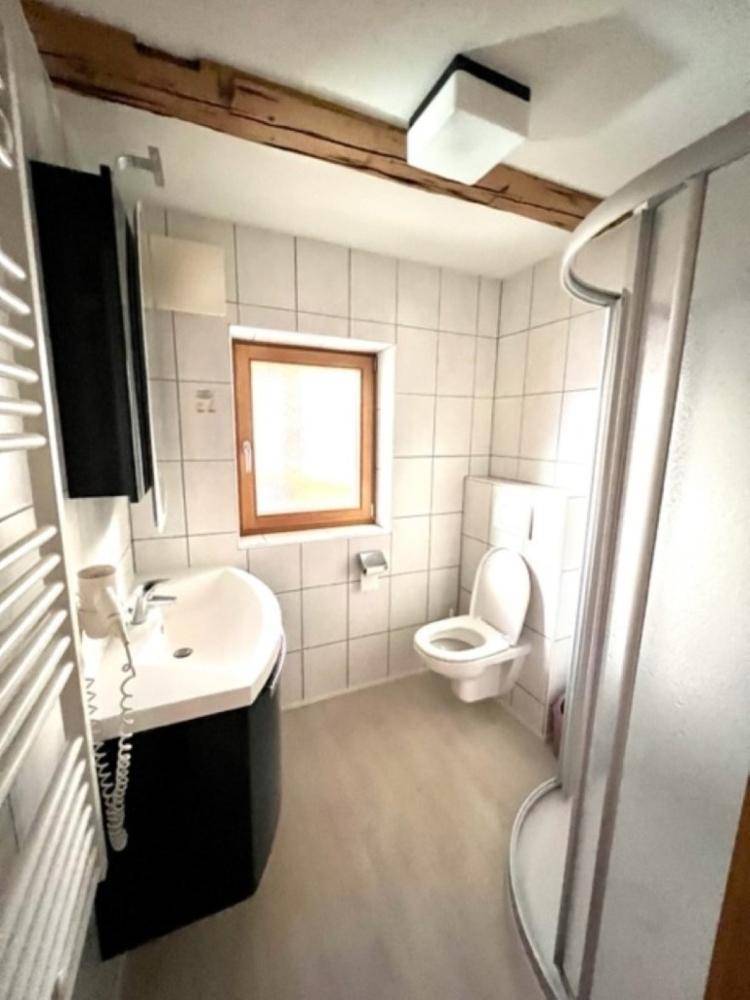 Helles Badezimmer mit Duschkabine, WC, Waschbecken und einem Fenster, ergänzt durch Holzbalken.