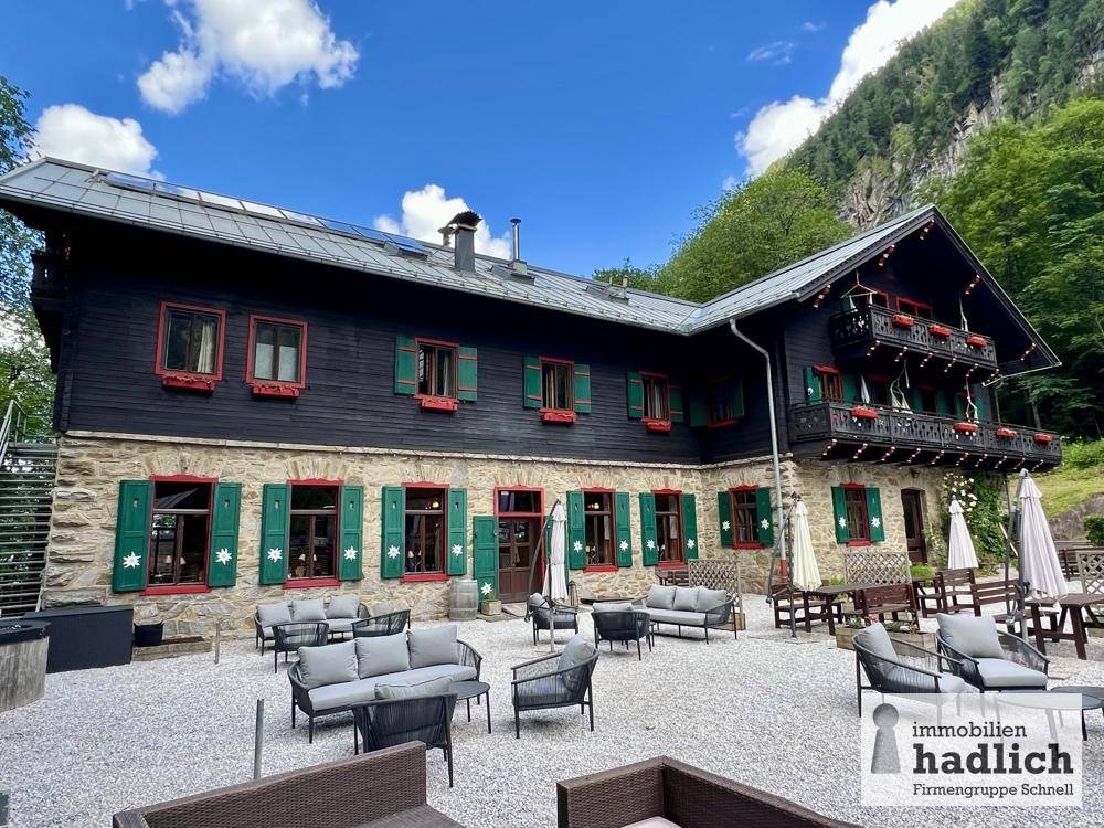 Große Außenterrasse mit modernen Sitzgelegenheiten vor einem traditionellen Gebäude mit Bergblick.