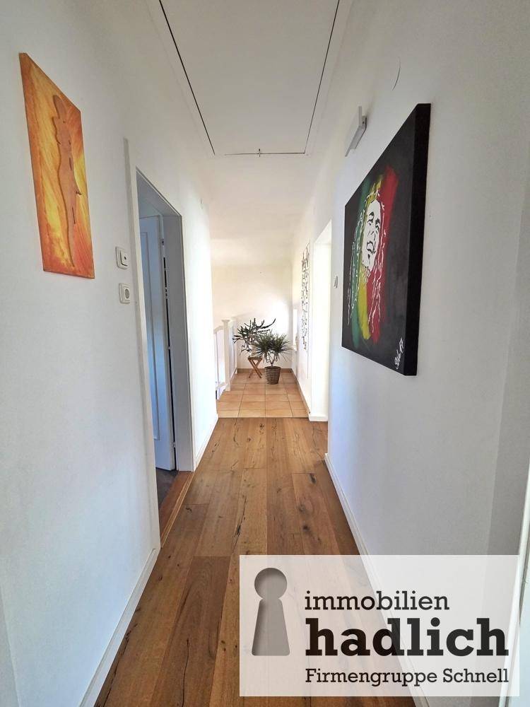 Langer Flur mit Holzboden, Kunstwerken an den Wänden und viel Licht.