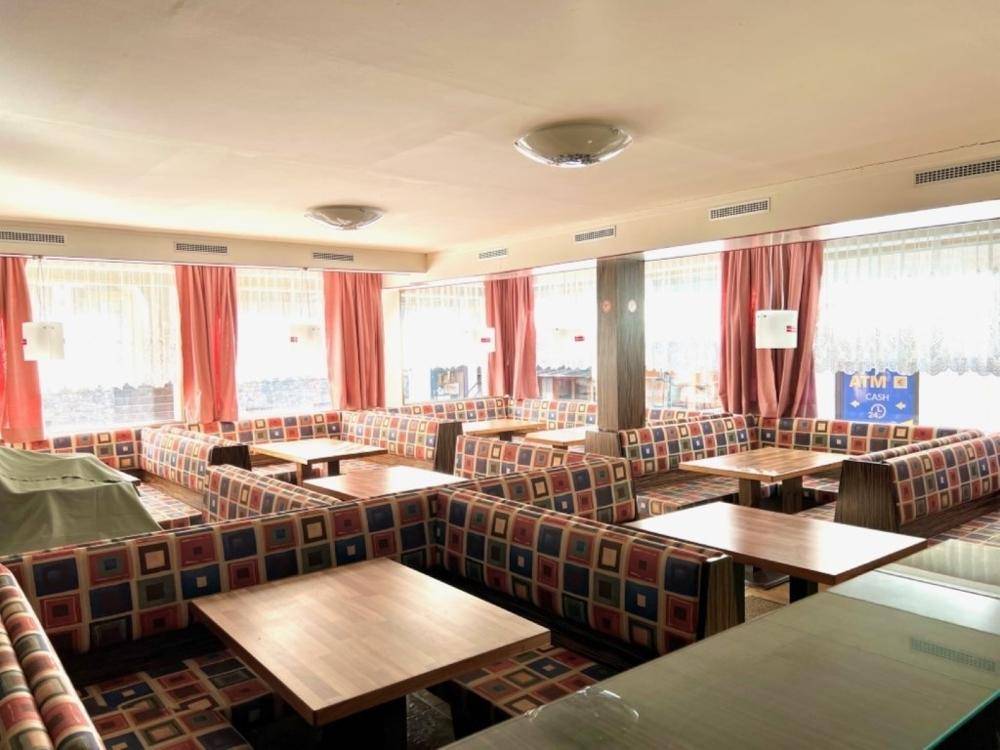 Geräumiger Restaurantbereich mit vielen Sitzgelegenheiten, Tischen und großen Fenstern mit roten Vorhängen.