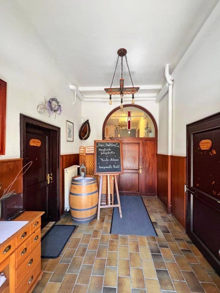 Eingangsbereich mit rustikalen Fliesen, Holztüren, einem dekorativen Fass und einer Kreidetafel.