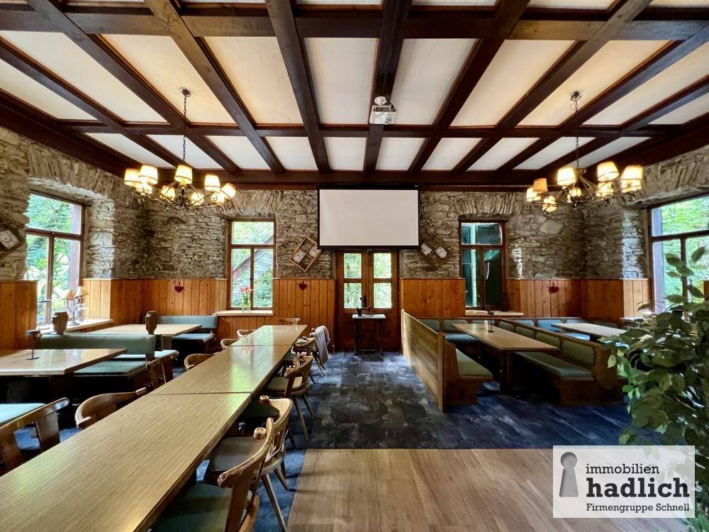 Geräumiger Speisesaal mit Holztischen, Bänken, Steinwänden und einer markanten Holzbalkendecke.