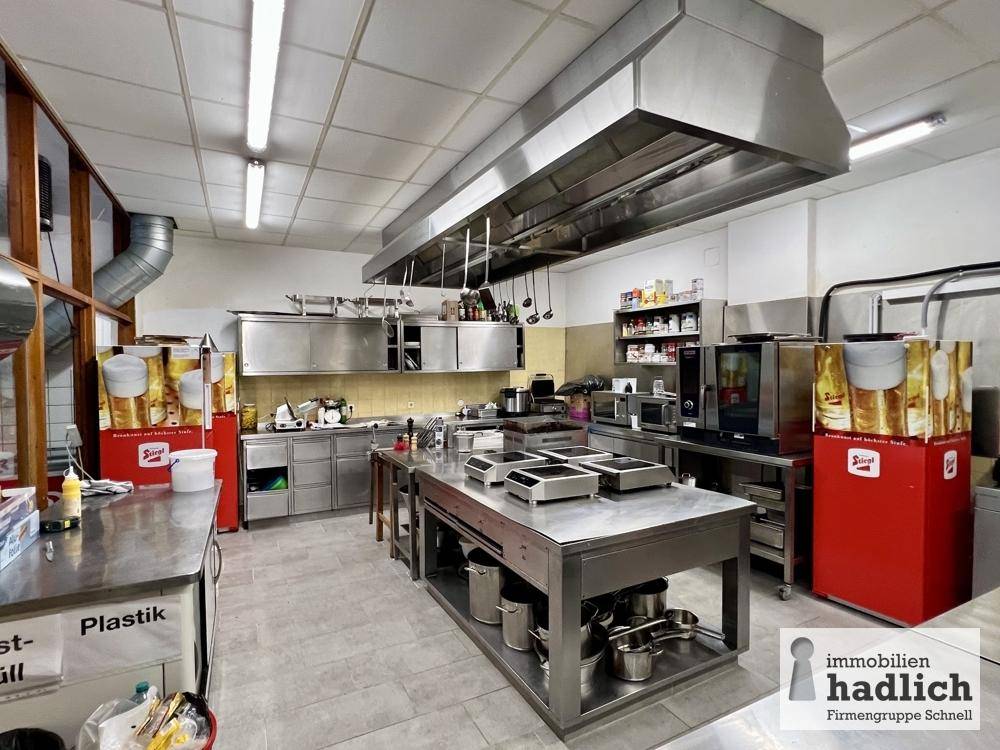 Große Industrieküche mit Edelstahlgeräten, Arbeitsflächen und einer leistungsstarken Dunstabzugshaube.